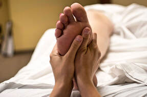 A picture of the bottom of a foot with a woman's hands massaging the bottom of the foot.