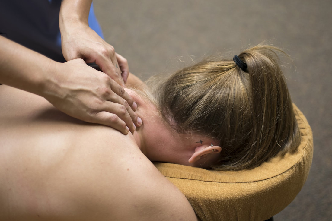 A picture of a woman lying face down with a massage therapist using her fingers to massage the shoulders.