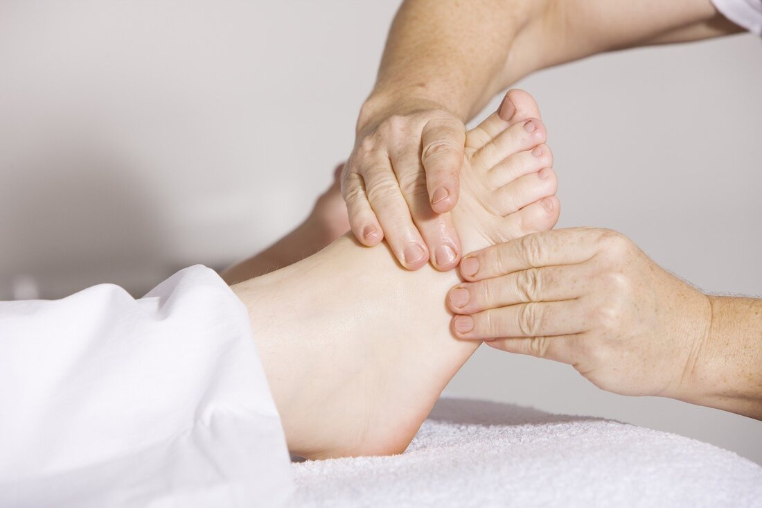A picture of the foot of a person lying on his back and another person's hands rubbing the foot.